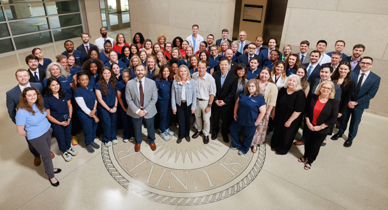 Ophthalmology Department group photo inside the School of Medicine. Bird's eye view. Group is standing on the School of Medicine emblem on the floor.